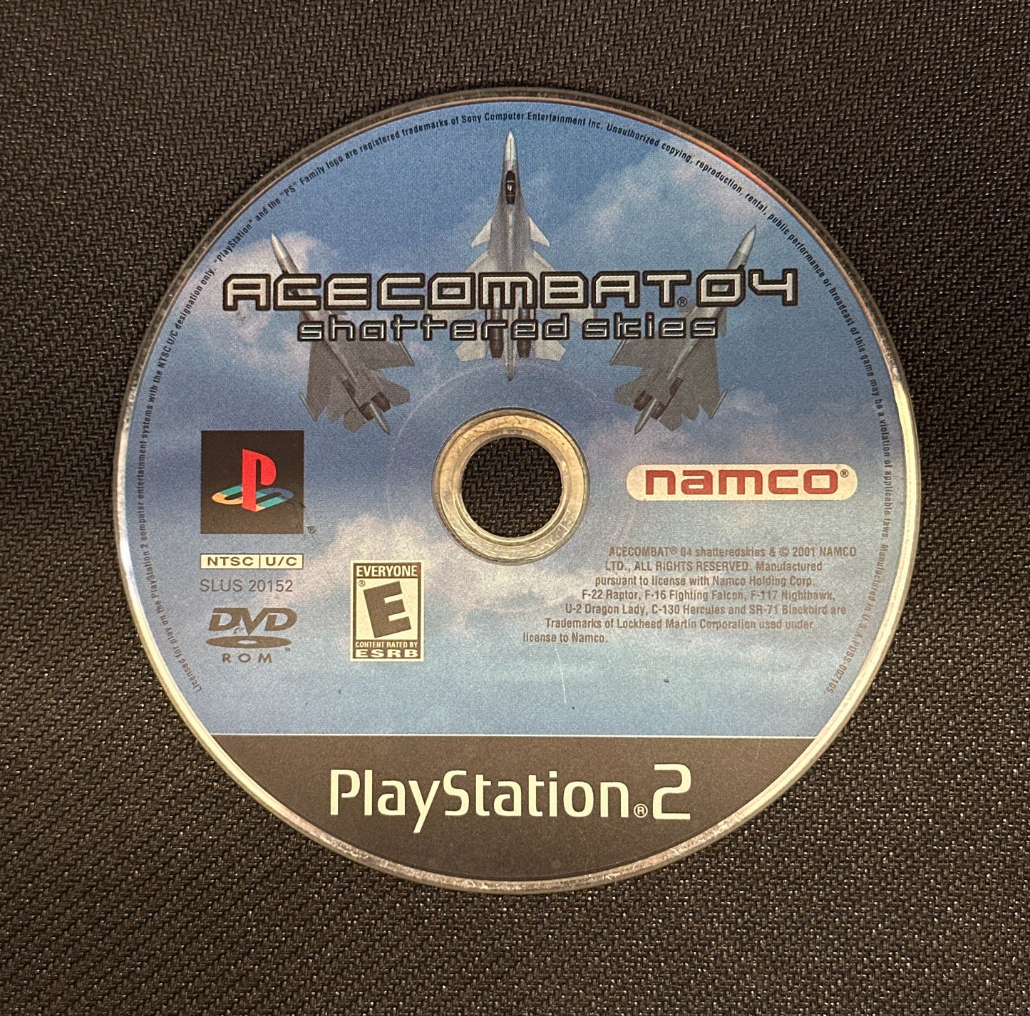 PlayStation 2 game disc for 'Ace Combat 04' on a textured black surface