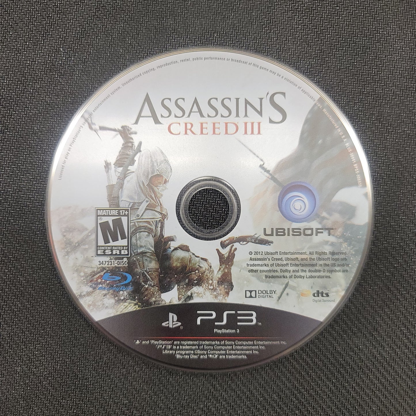 Assassin's Creed III game disc on a textured surface