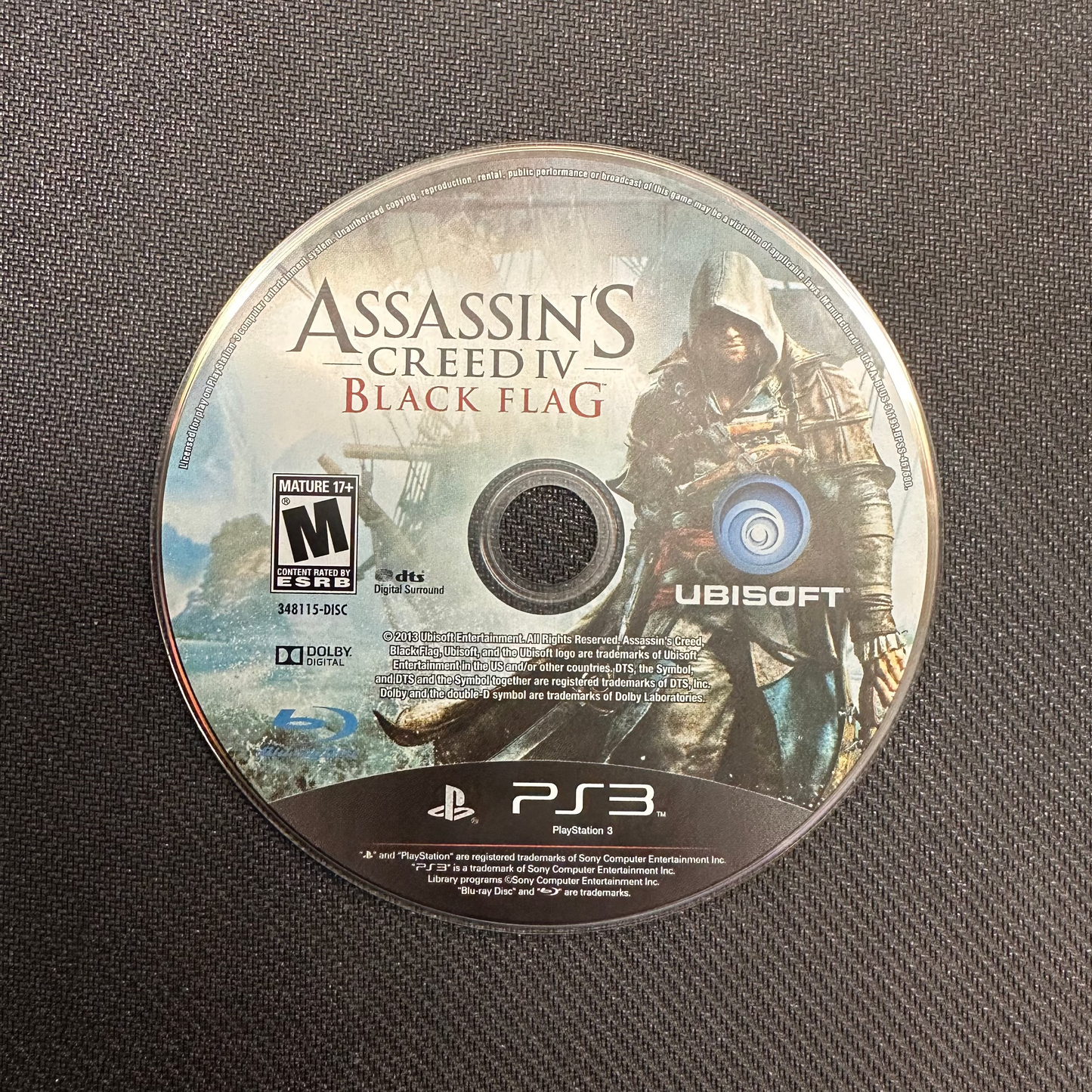 Assassin's Creed IV Black Flag game disc on a textured surface