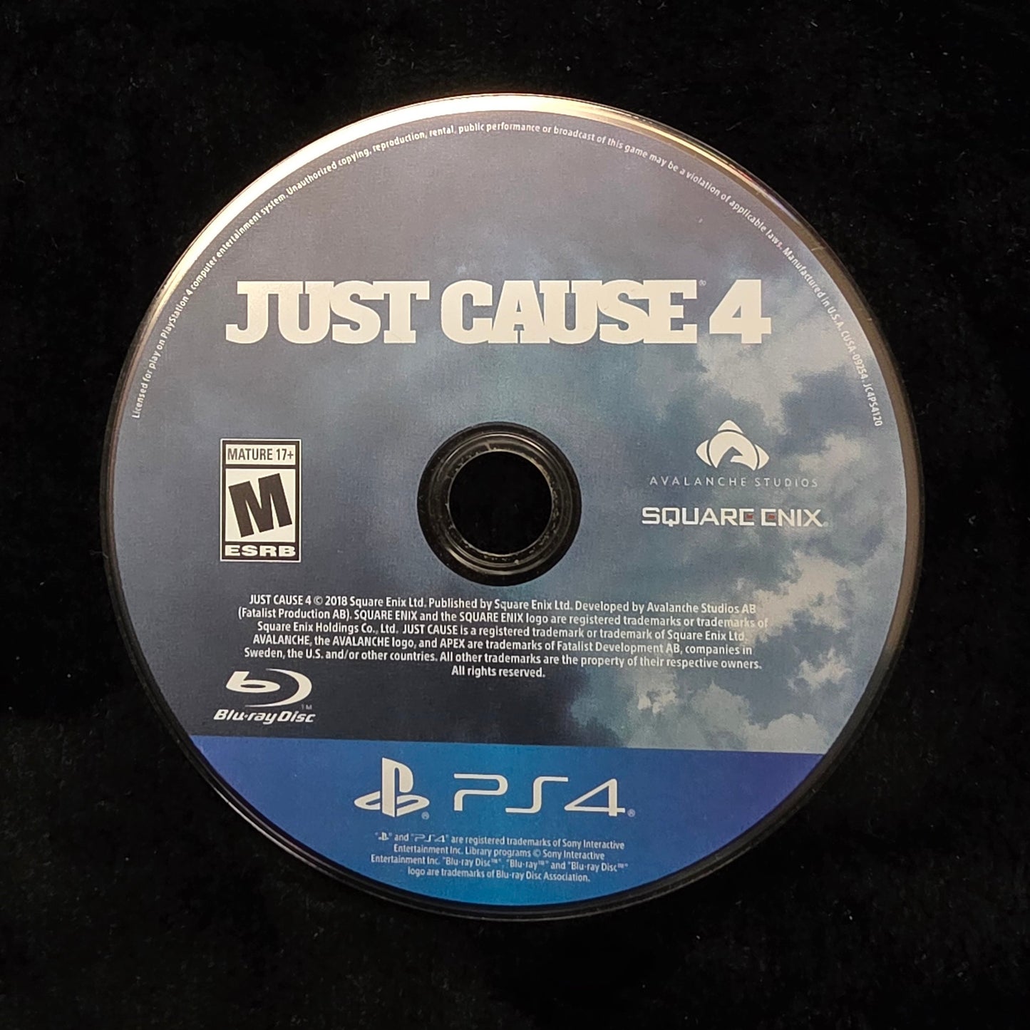 A PlayStation 4 Blu-ray disc for the video game Just Cause 4, resting on a black textured surface.