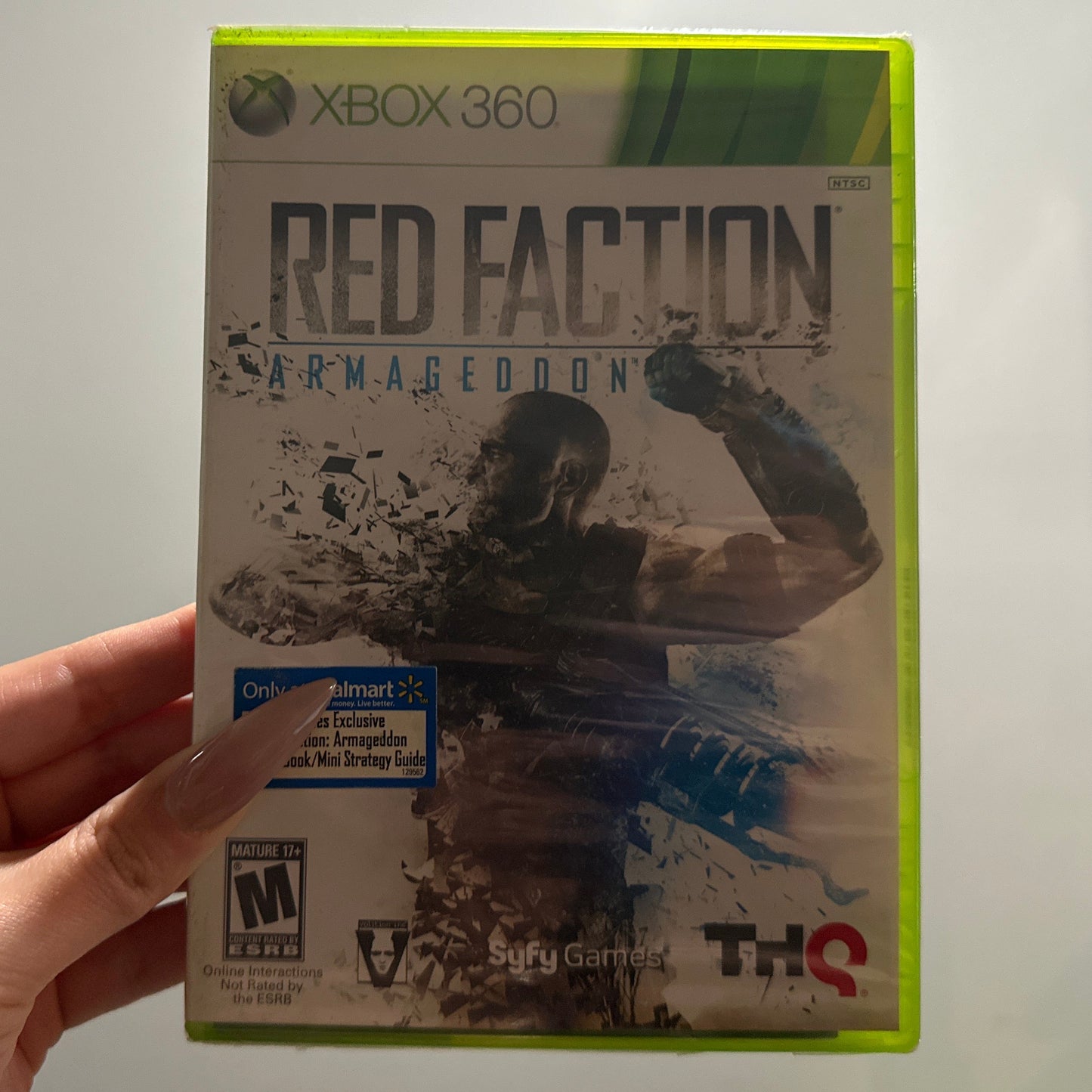 Xbox 360 game case titled 'Red Faction: Armageddon' held by a hand against a neutral background.