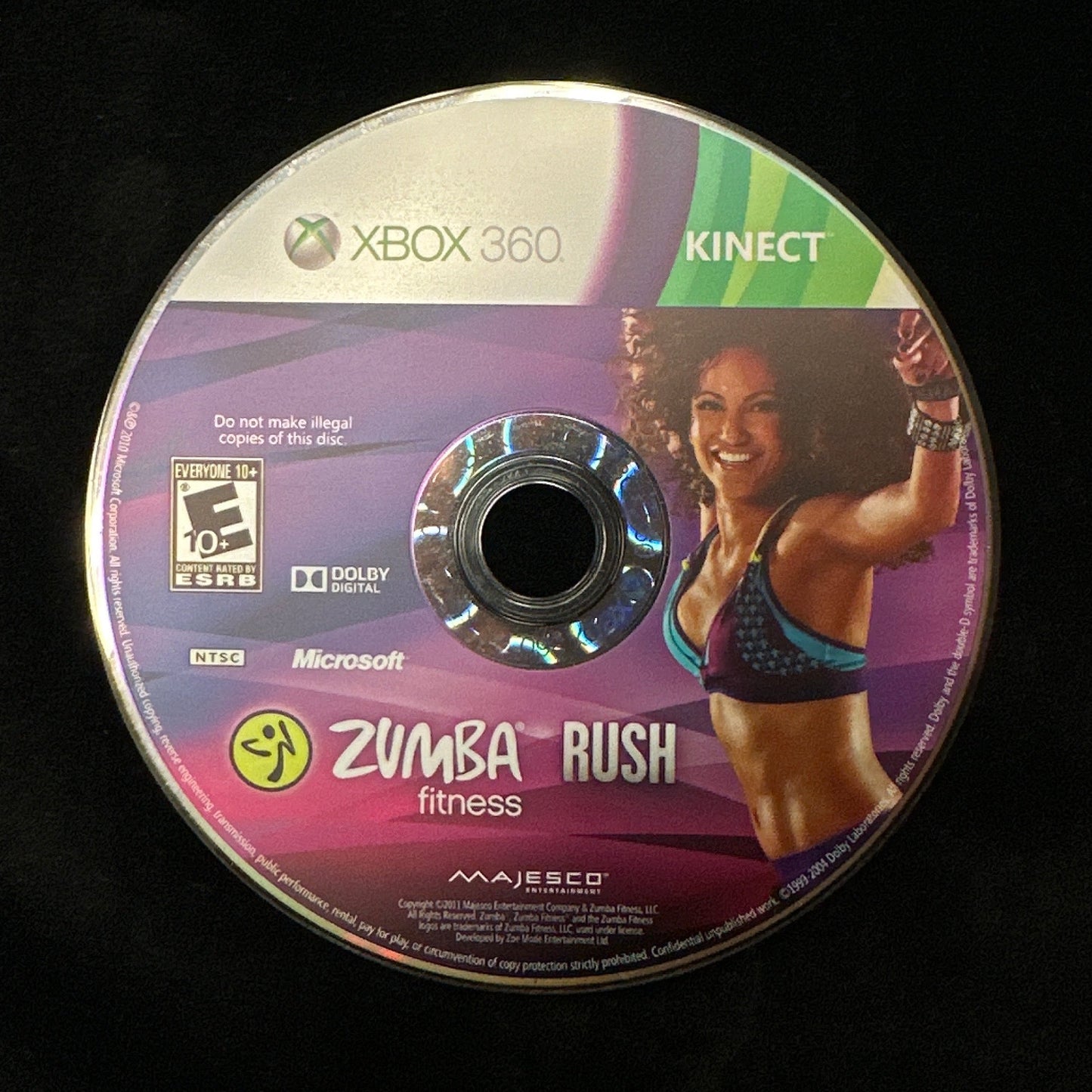 A used Xbox 360 Kinect Zumba Rush fitness game disc resting on a black fabric surface.