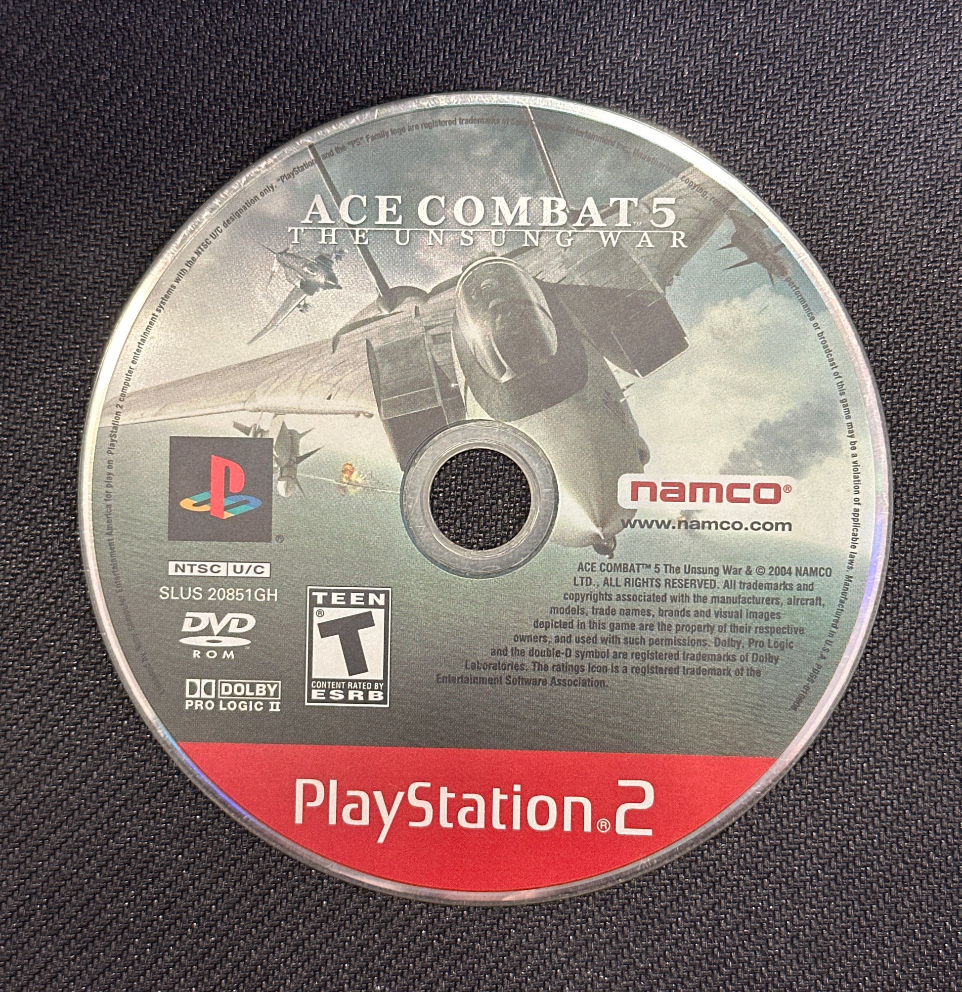 PlayStation 2 game disc for 'Ace Combat 5' on a dark textured background