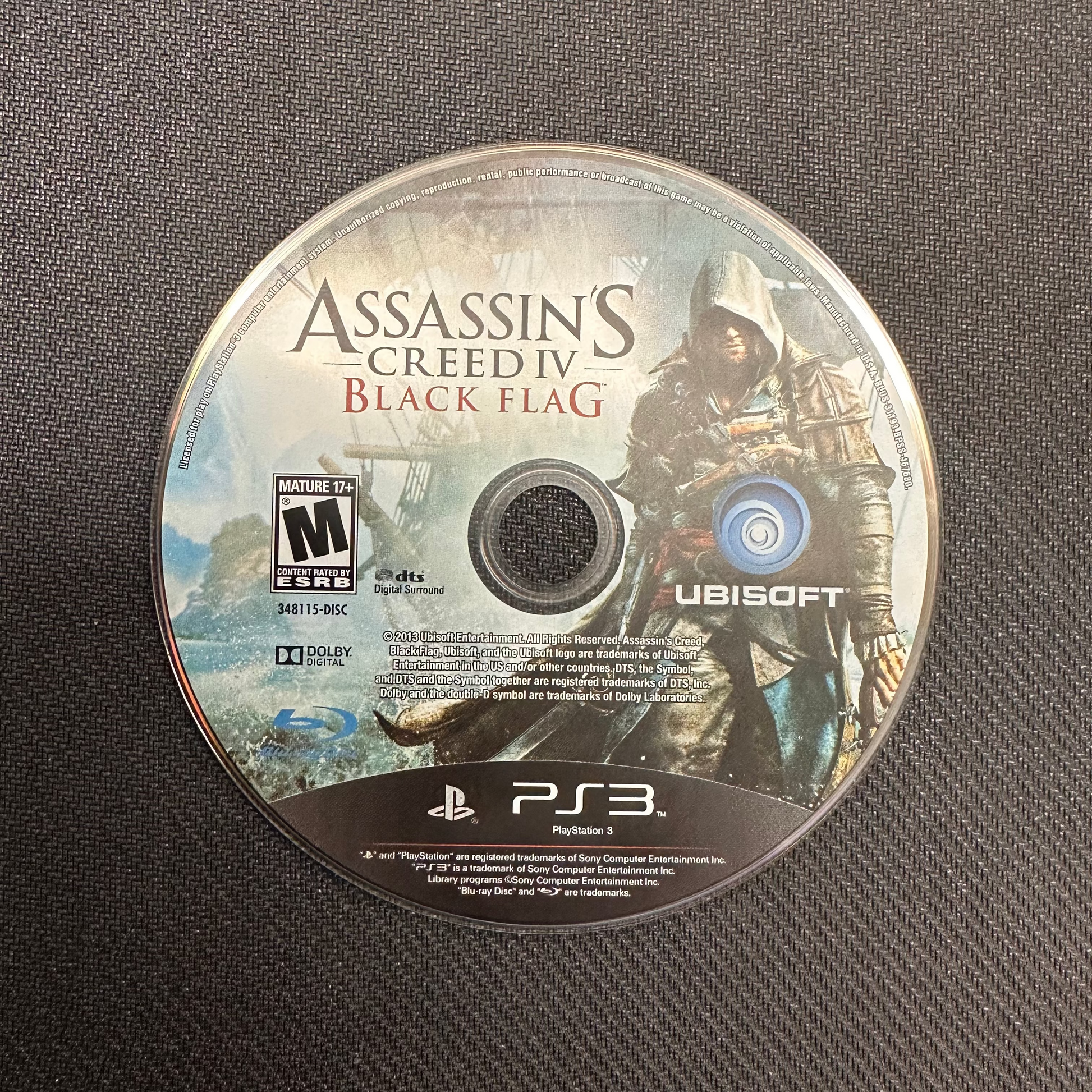 Assassin's Creed IV Black Flag game disc on a textured surface