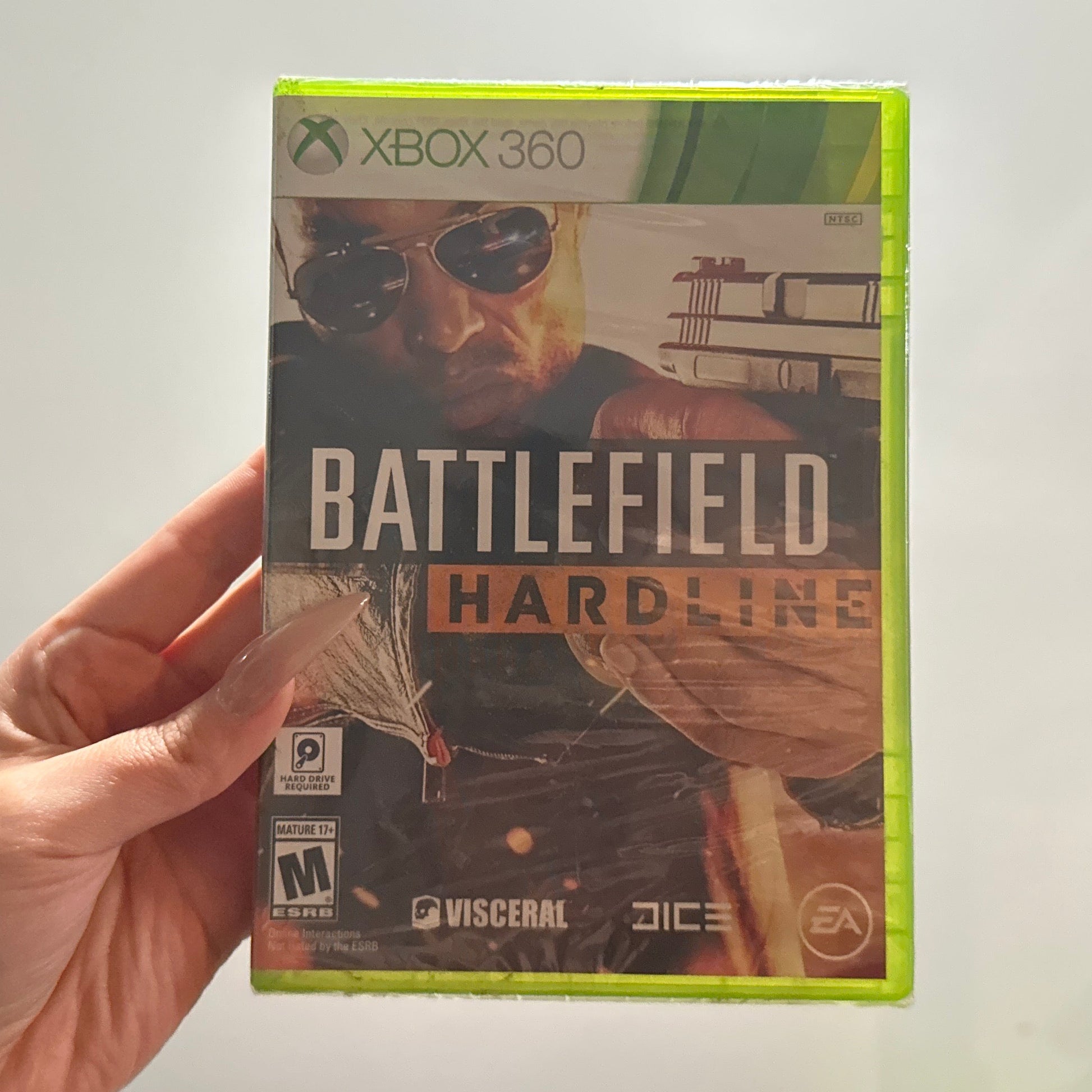 Hand holding a 'Battlefield Hardline' Xbox 360 game case against a neutral background