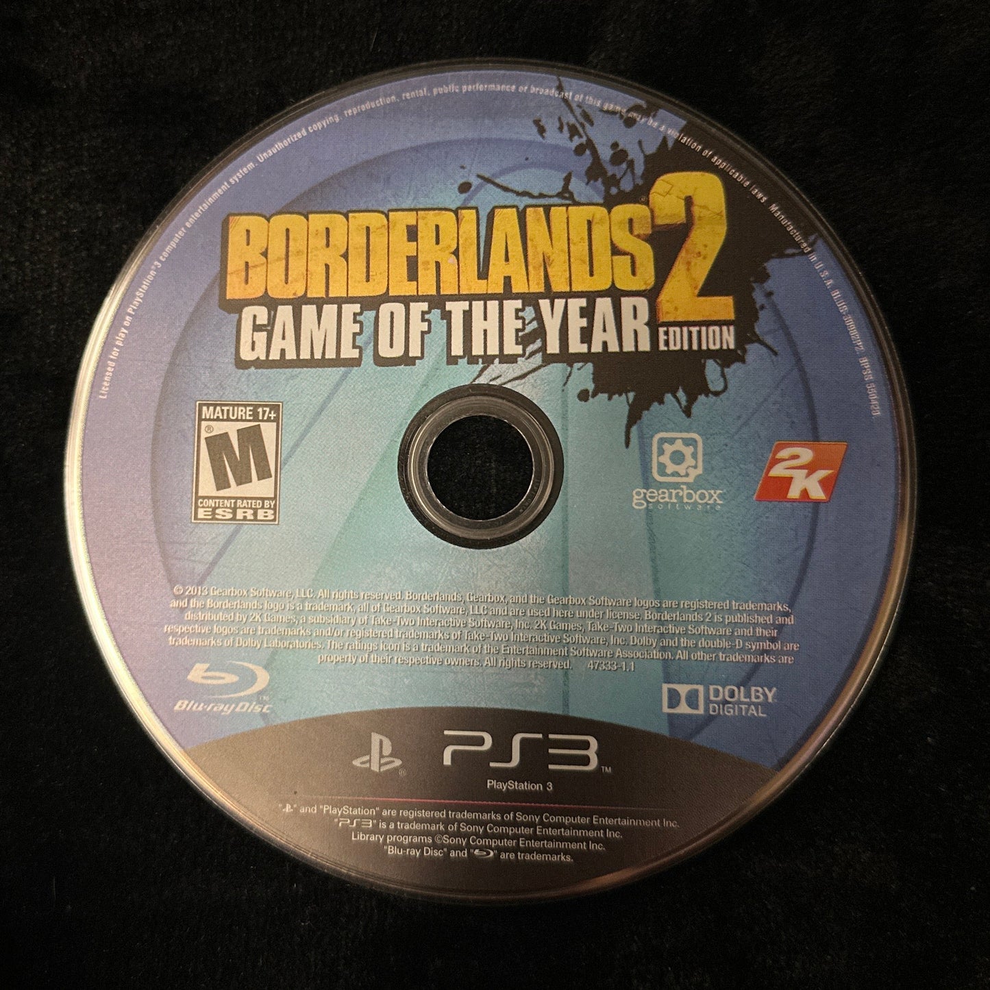A PlayStation 3 game disc for Borderlands 2: Game of the Year Edition, resting on a black textured fabric surface.