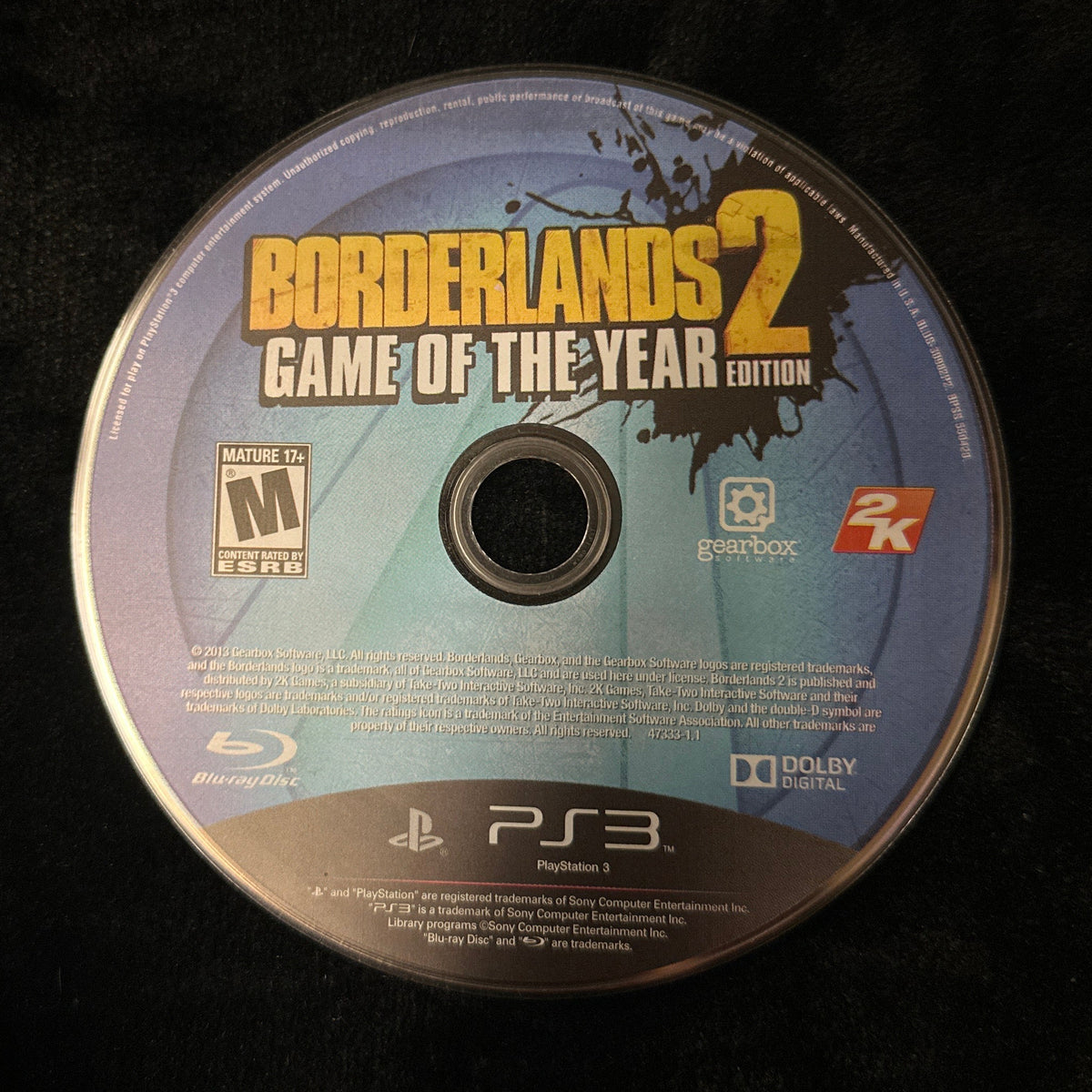 A PlayStation 3 game disc for Borderlands 2: Game of the Year Edition, resting on a black textured fabric surface.