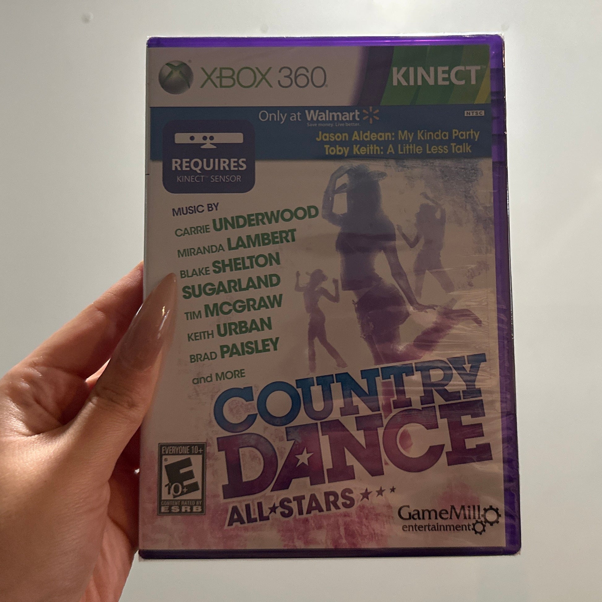 Hand holding a 'Country Dance All-Stars' game case for Xbox 360 Kinect against a neutral background.