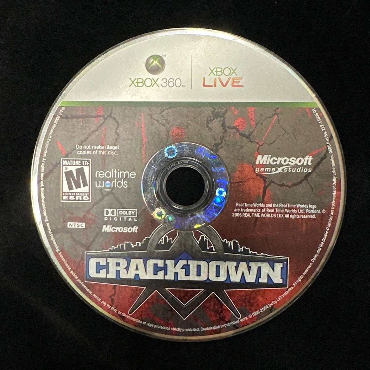 An Xbox 360 game disc for the video game Crackdown, featuring Microsoft and Xbox branding, resting on a black textured fabric background.