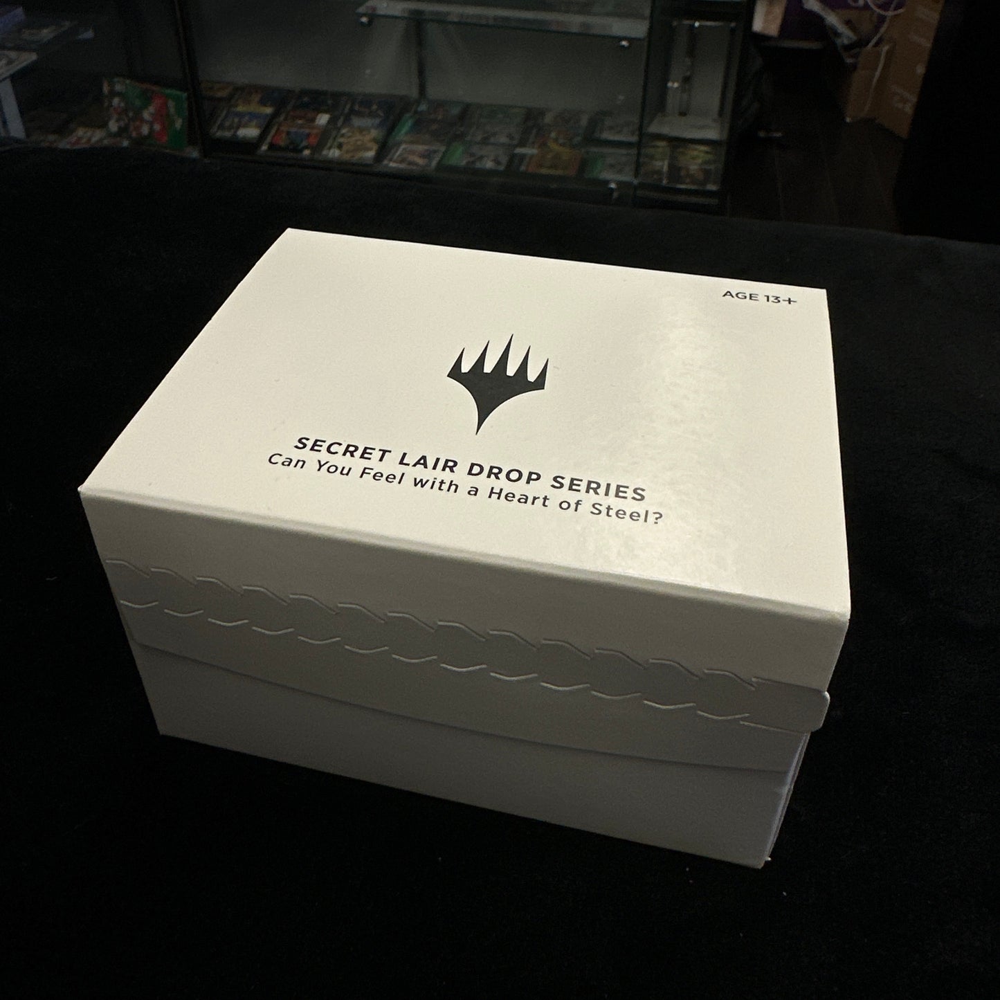 White box with text and mtg logo on a black surface in a store setting