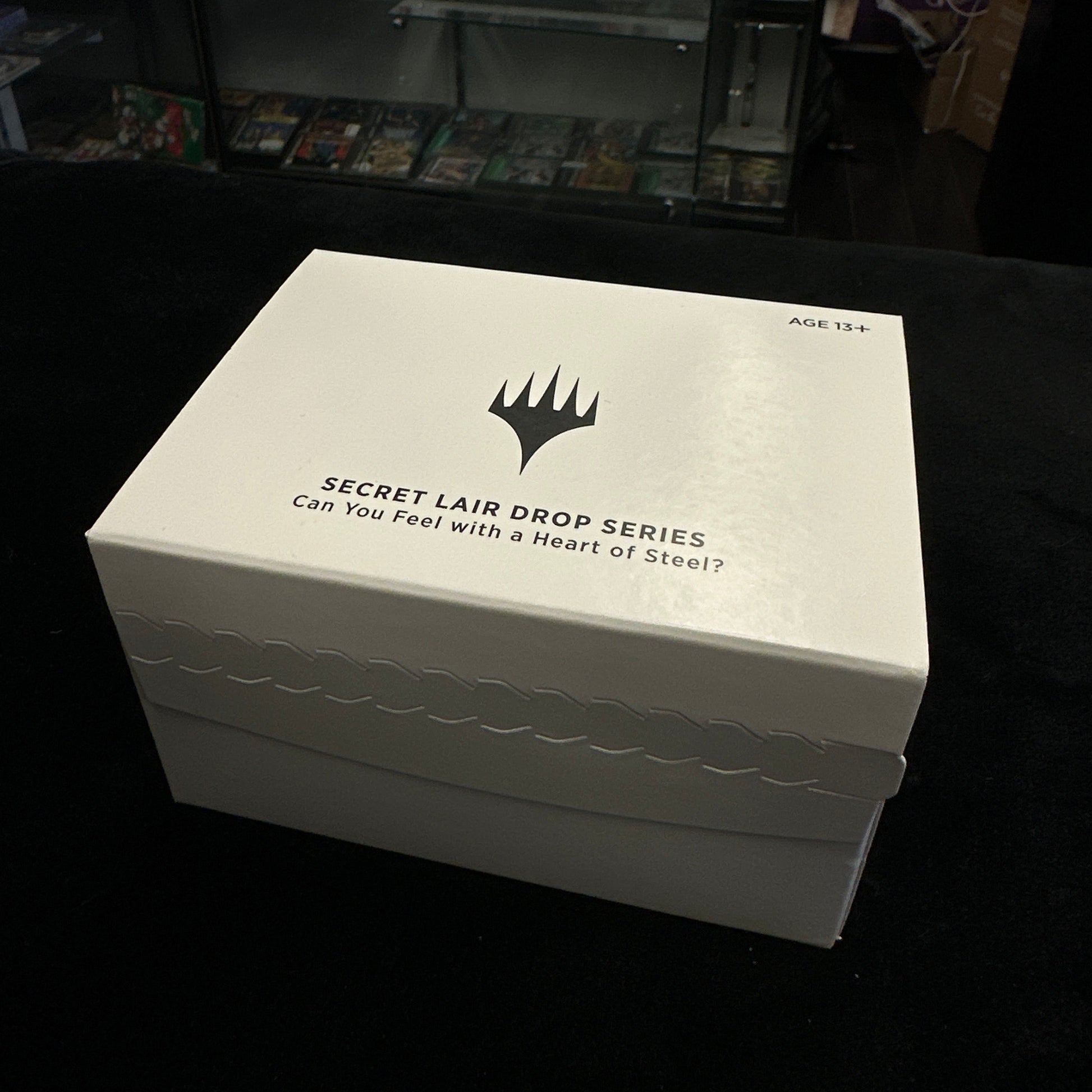 White box with text and mtg logo on a black surface in a store setting