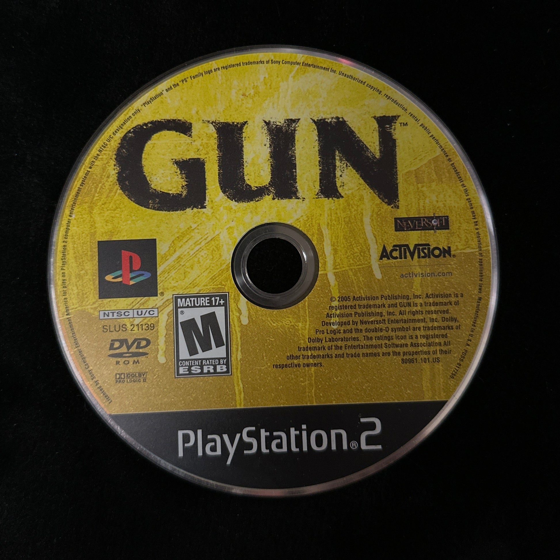 A PlayStation 2 game disc for the game 'Gun' on a black fabric surface, showing the yellow cover art and PlayStation branding.
