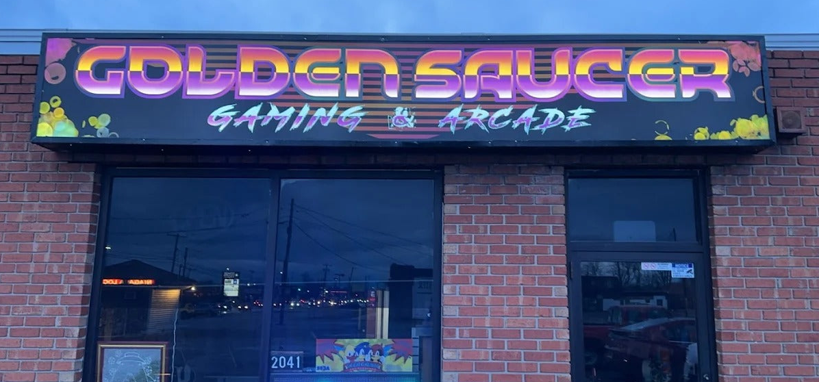  storefront sign for 'Golden Saucer Gaming & Arcade' with colorful text on a brick building.