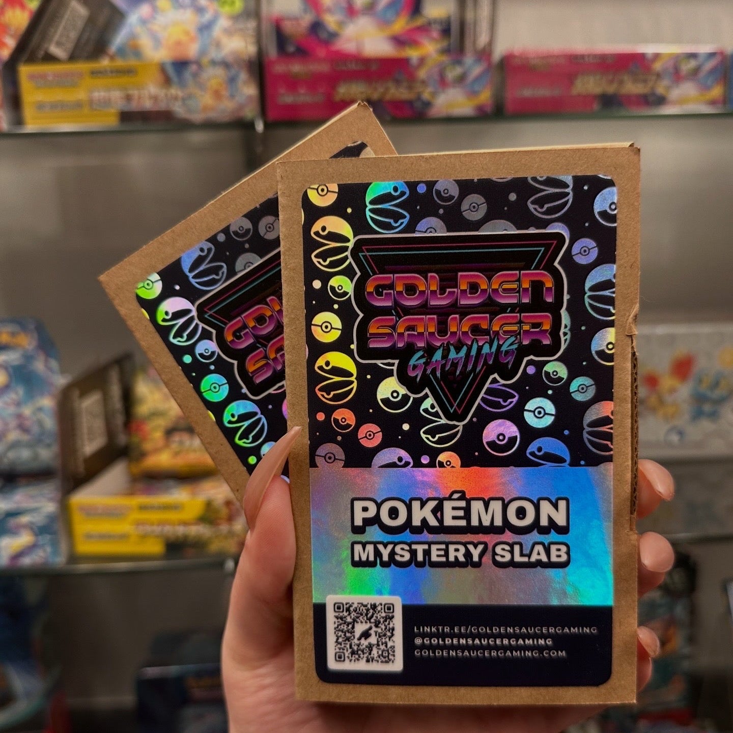 Pokémon Mystery Slab packaging held by a person with colorful boxes in the background