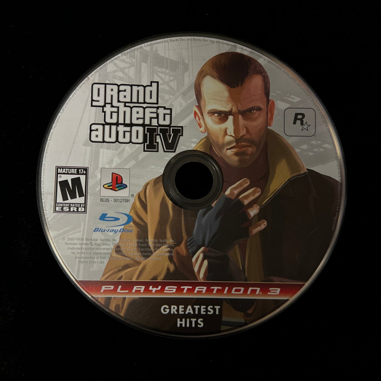 A PlayStation 3 Greatest Hits Grand Theft Auto IV Blu-ray game disc shown against a solid black background.