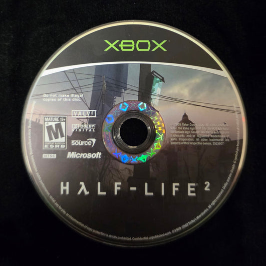 An Xbox Half-Life 2 game disc resting on a black fabric surface, with the Xbox logo and Half-Life 2 title clearly visible.