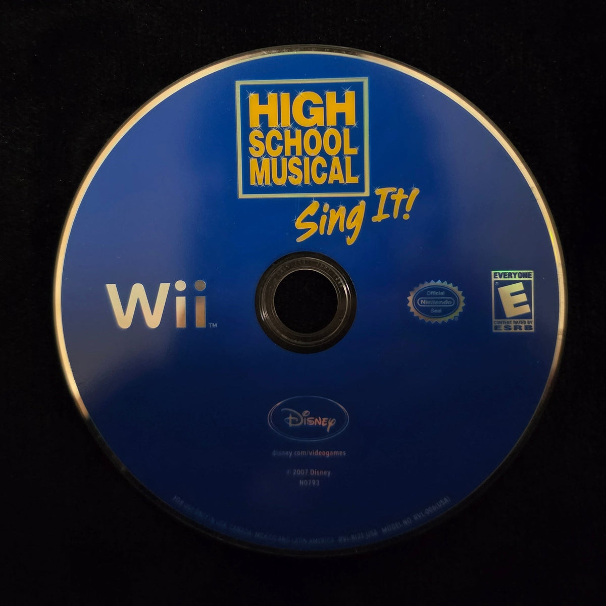 A blue Nintendo Wii game disc for Disney's High School Musical: Sing It! on the Wii, resting on a black surface.