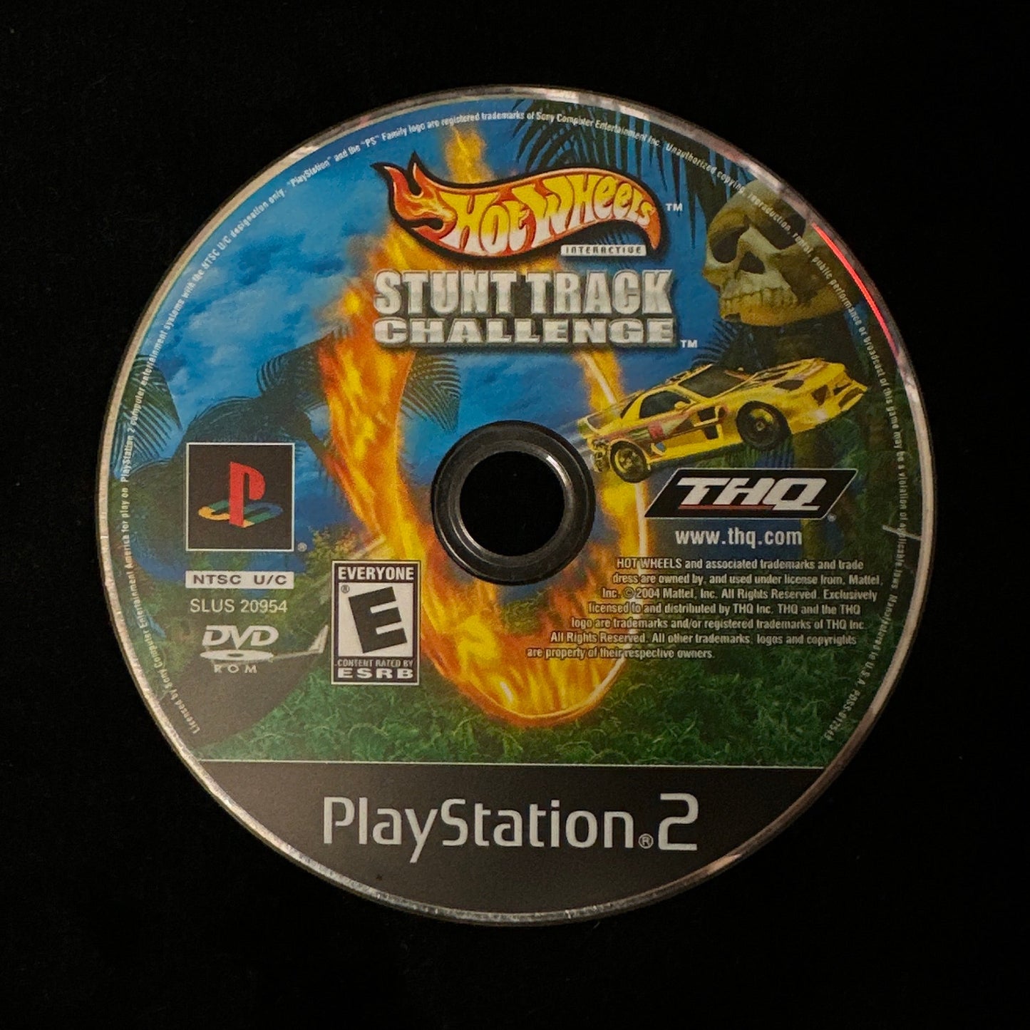 A PlayStation 2 DVD game disc for Hot Wheels Stunt Track Challenge, featuring a colorful label with flames, a yellow race car, and PlayStation and THQ logos, photographed on a black background.