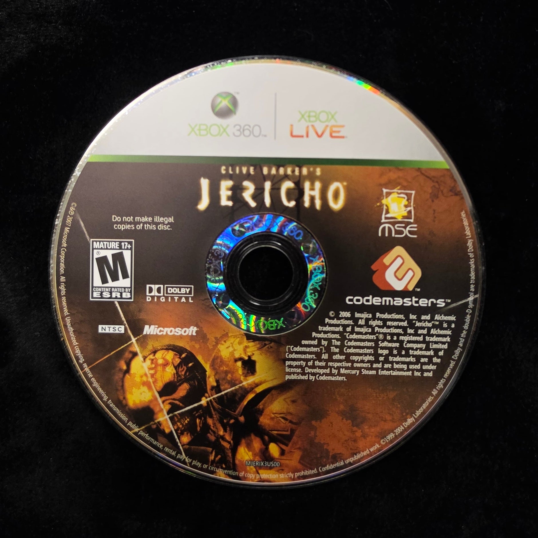 A used Xbox 360 disc of Clive Barker's Jericho, showing the front cover art and Xbox Live branding, resting on a black surface.