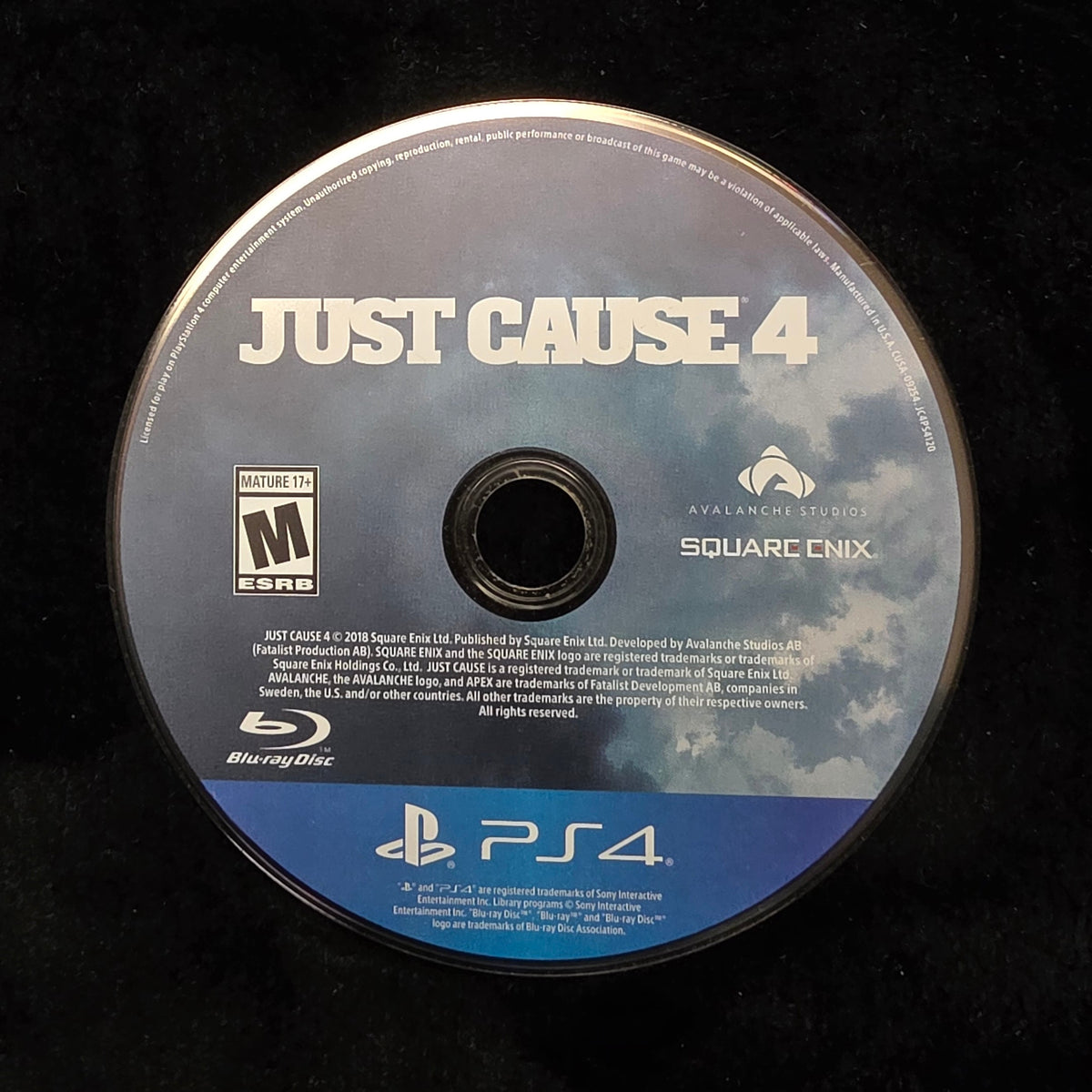 A PlayStation 4 Blu-ray disc for the video game Just Cause 4, resting on a black textured surface.