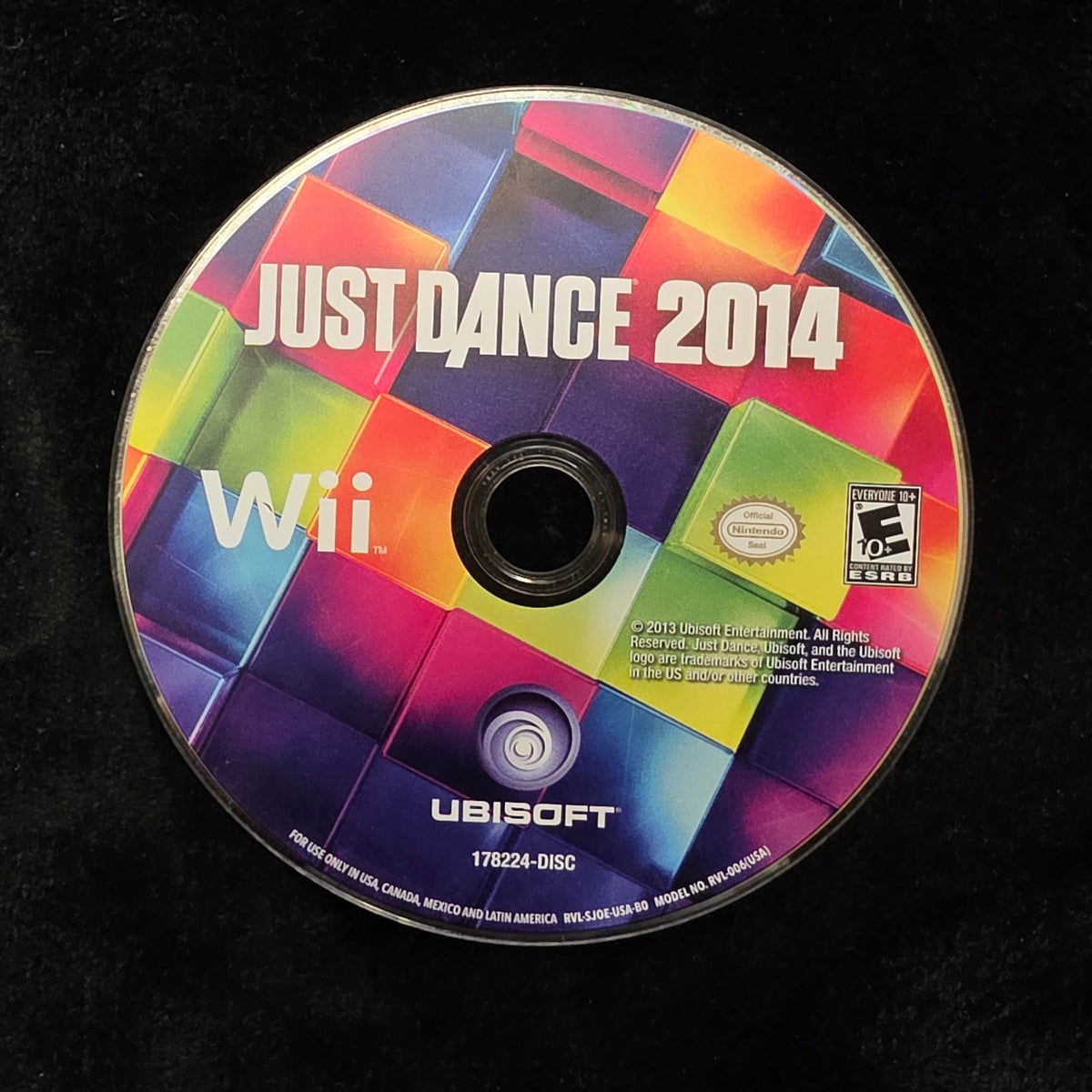 A used Nintendo Wii game disc for Just Dance 2014, featuring the colorful game cover art, resting on a black fabric surface.
