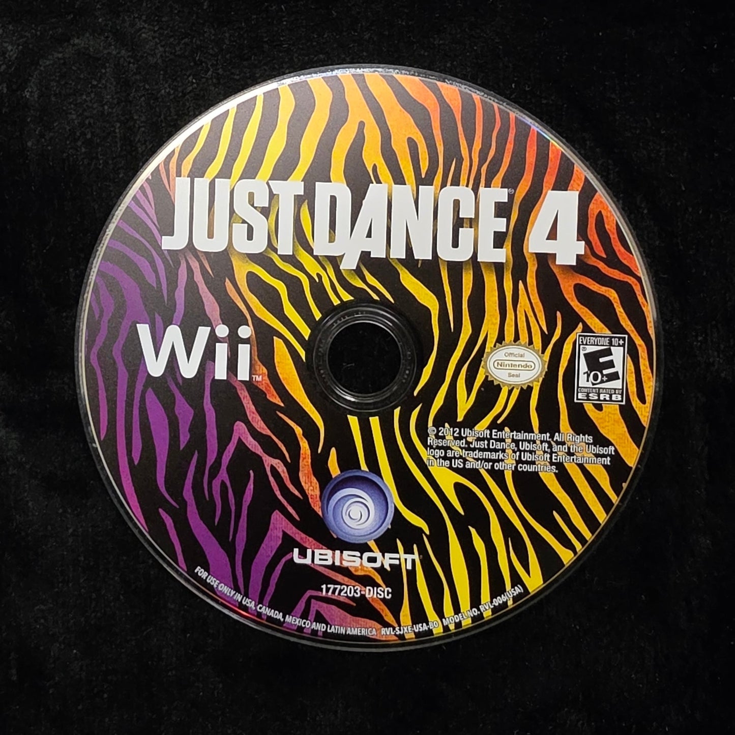 A Wii game disc for Just Dance 4, featuring a vibrant zebra-stripe pattern in yellow, orange, red, purple, and black, resting on a black fabric surface.