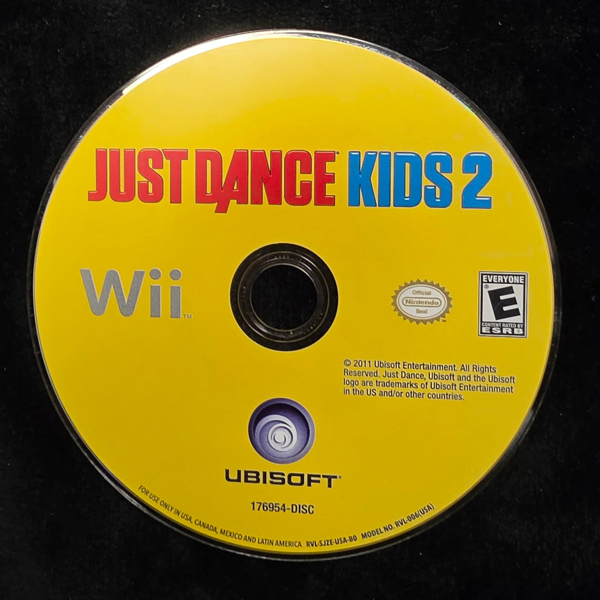 A yellow Nintendo Wii game disc for Just Dance Kids 2, featuring red and blue title text, resting on a black textured surface.