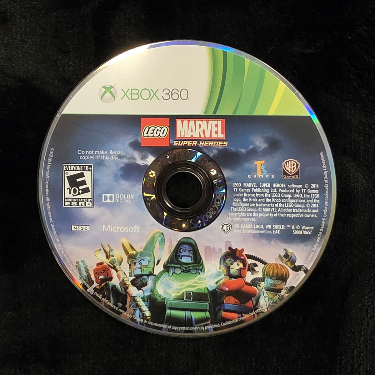 A used Xbox 360 LEGO Marvel video game disc resting on a black fabric surface.