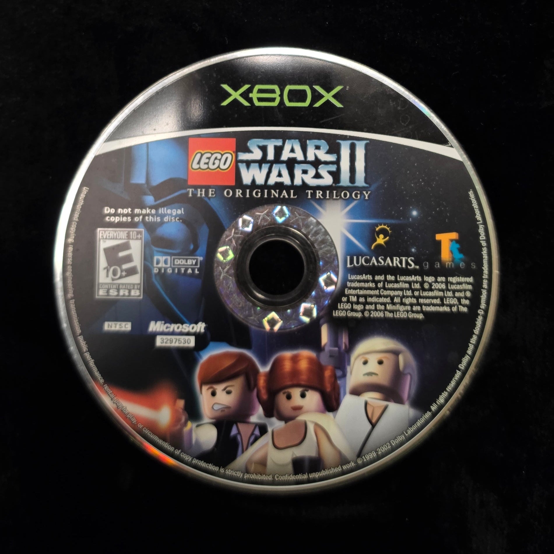 A used Xbox disc for LEGO Star Wars II: The Original Trilogy, displayed on a black fabric surface.
