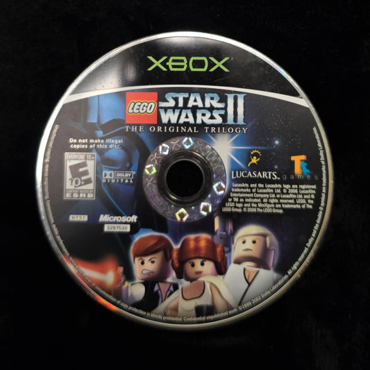 A used Xbox disc for LEGO Star Wars II: The Original Trilogy, displayed on a black fabric surface.