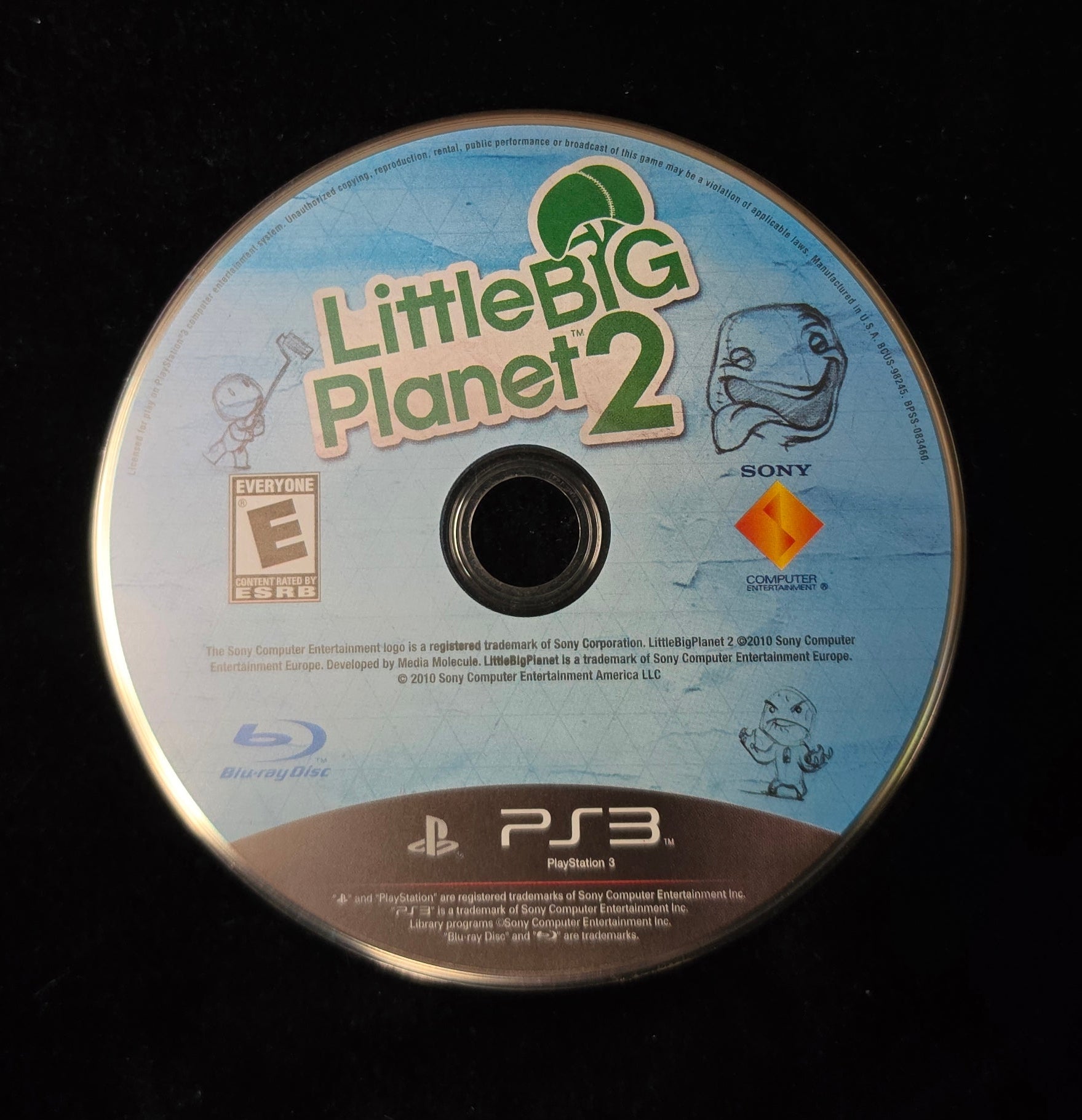 A PlayStation 3 disc for the video game LittleBig Planet 2, resting on a black fabric surface.