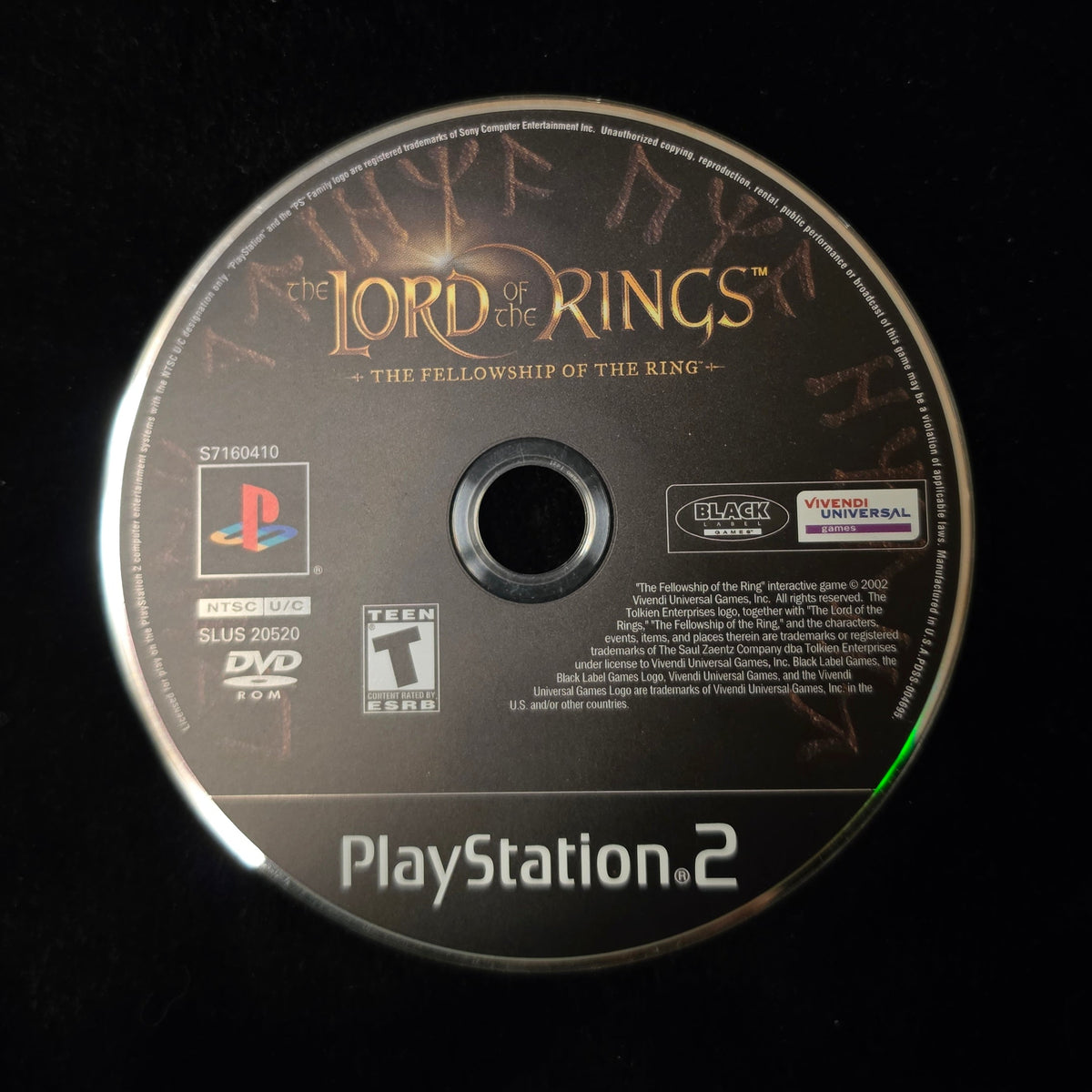A PlayStation 2 game disc for 'Lord of the Rings: The Fellowship of the Ring' resting on a black fabric surface.