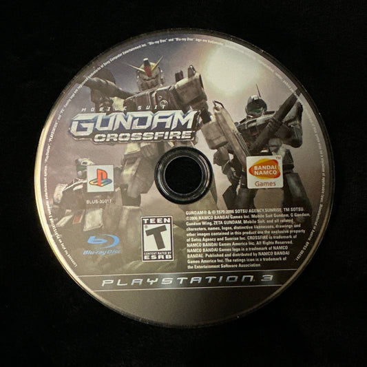 A PlayStation 3 game disc for Gundam Crossfire resting on a black fabric surface.