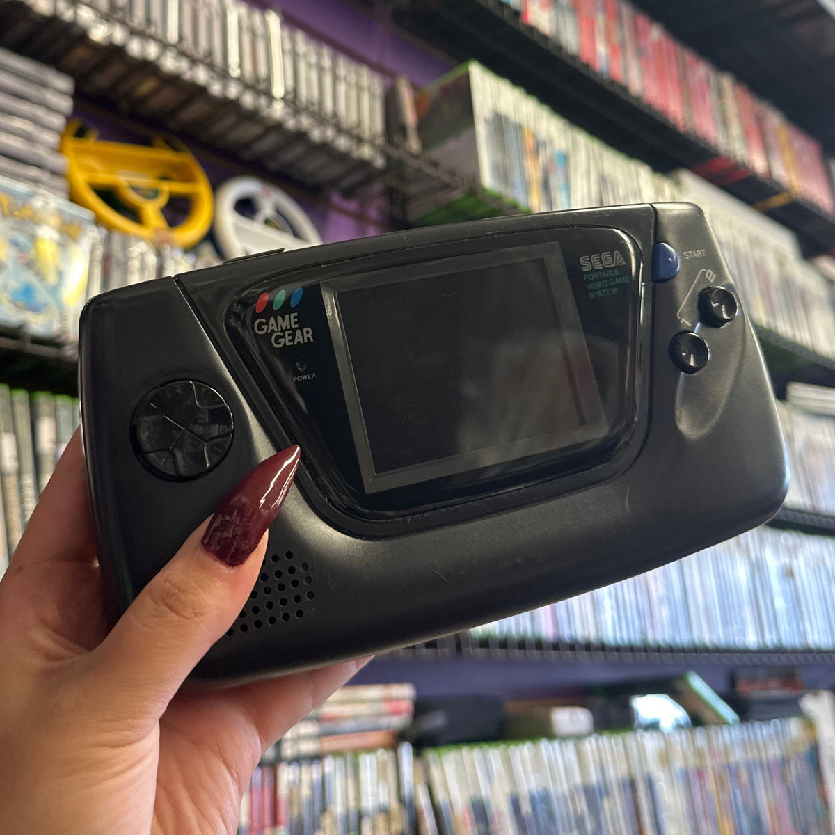 Sega Game Gear Handheld Gaming Console held in hand in front of a walk of video game cases