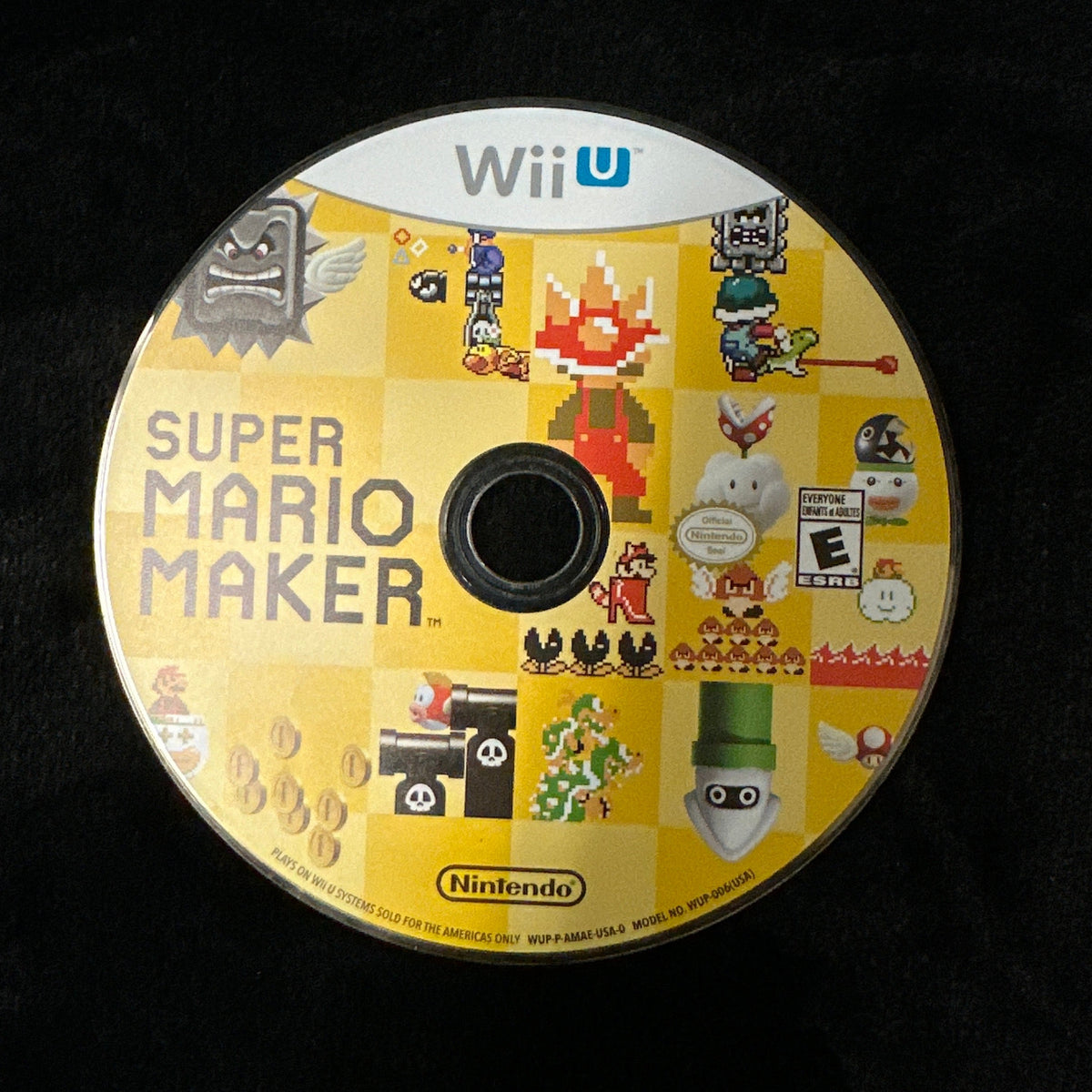 A yellow Nintendo Wii U Super Mario Maker game disc resting on a black fabric surface.