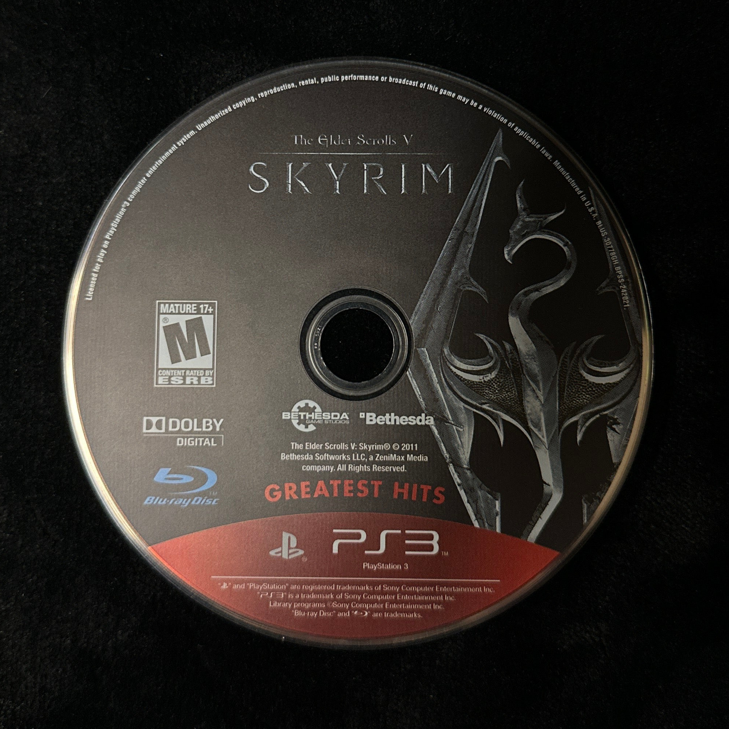 A PlayStation 3 Skyrim Greatest Hits Blu-ray game disc resting on a black surface