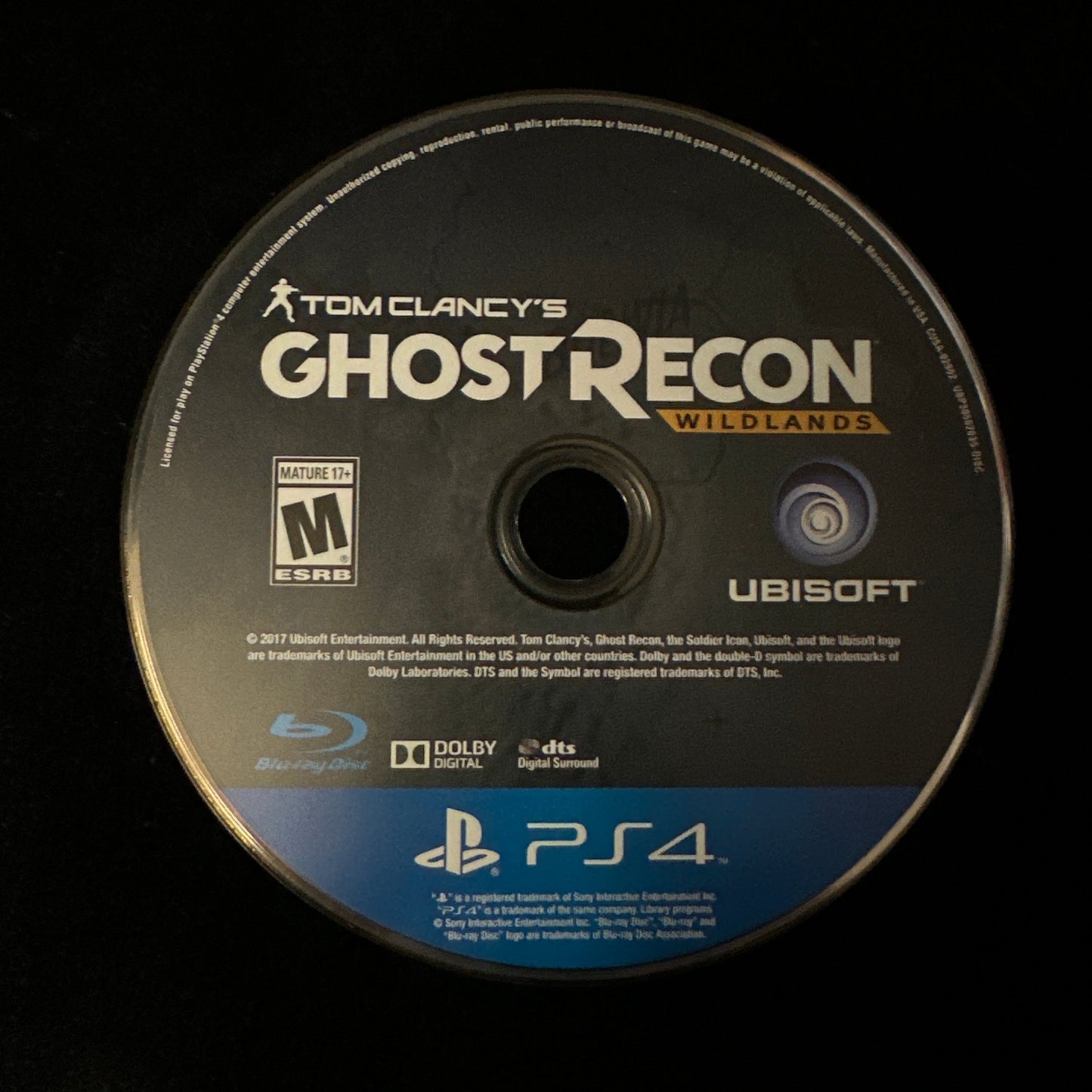 A Tom Clancy's Ghost Recon Wildlands PS4 game disc for PlayStation 4, featuring Ubisoft branding and a blue PS4 banner at the bottom, photographed on a black background.