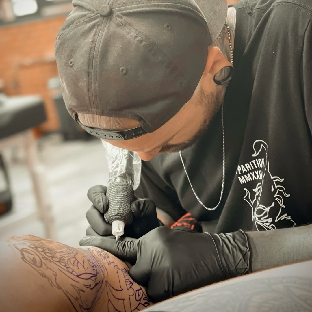 Tattoo artist working on a client's arm with a tattoo machine.